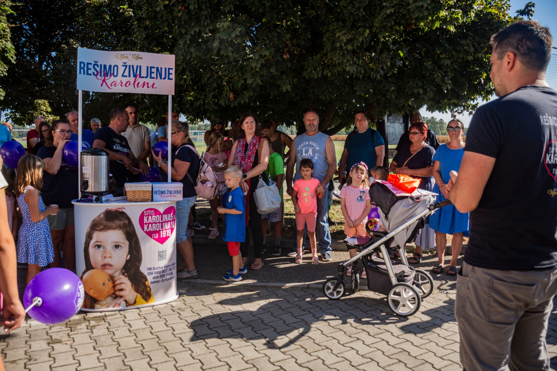 Množica pred humanitarno stojnico v senci dreves