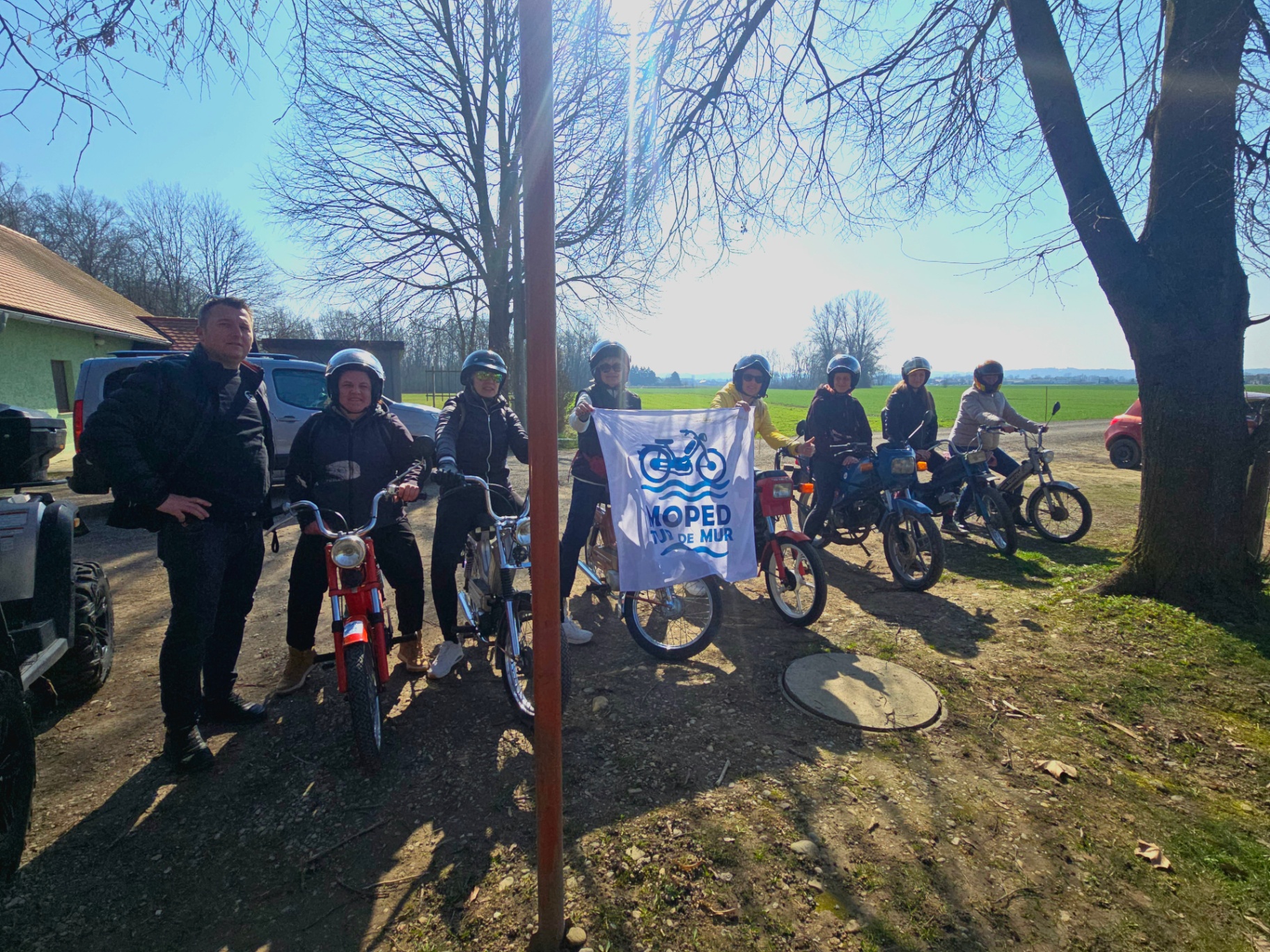 Udeleženci z zastavo MOPED Mur pod pomladnim drevesom