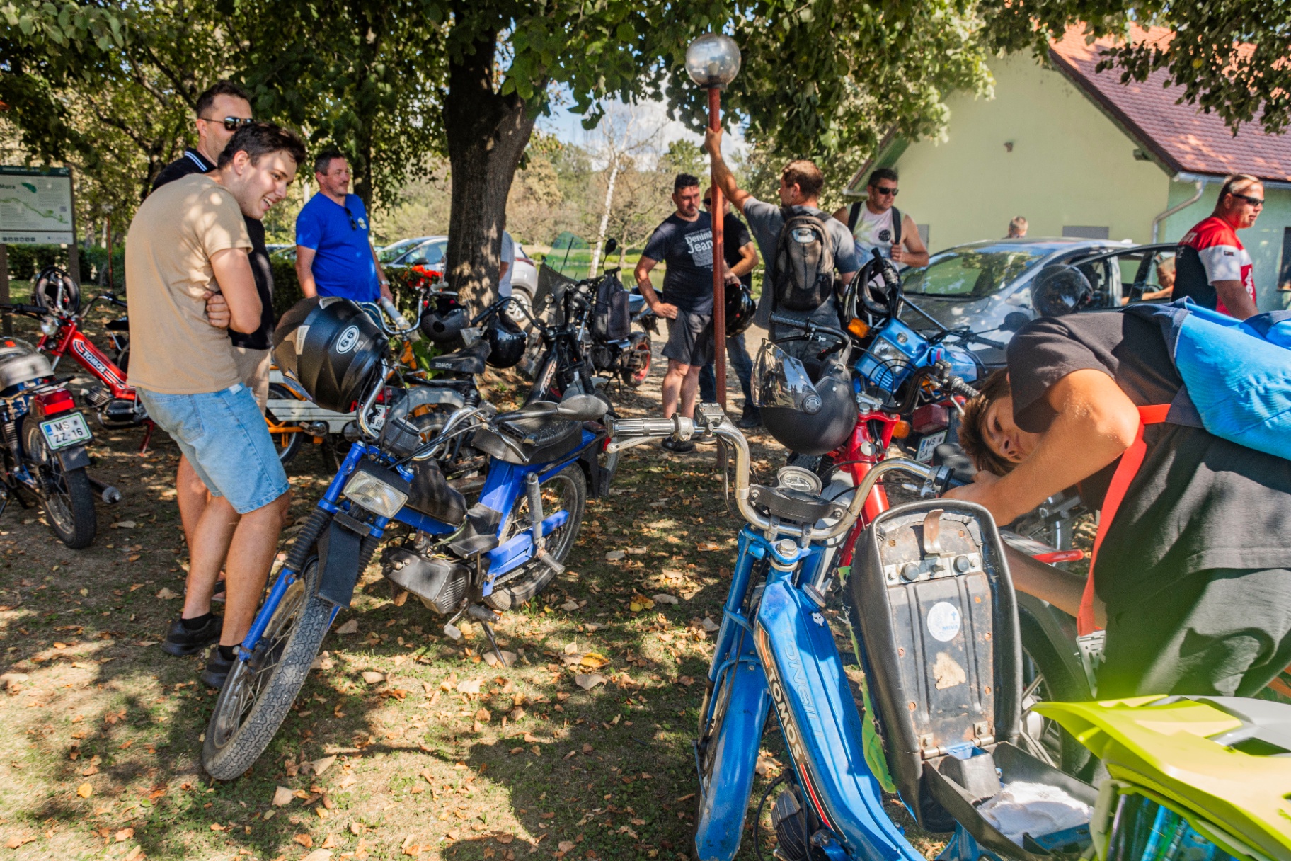 Udeleženci počivajo med parkiranimi mopedi v senci dreves