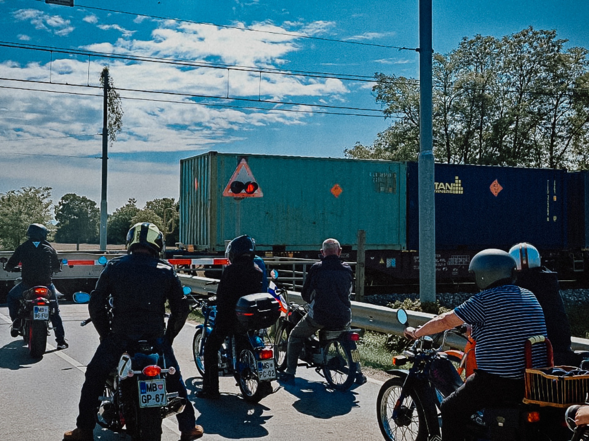 Kolona mopedistov čaka ob spuščeni železniški zapornici med vožnjo