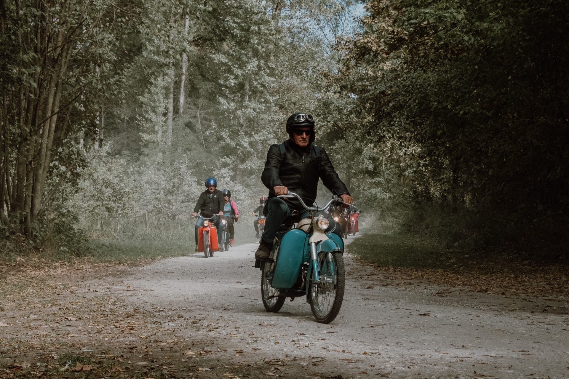 Vintage moped v ospredju vodi kolono po beli makadamski poti