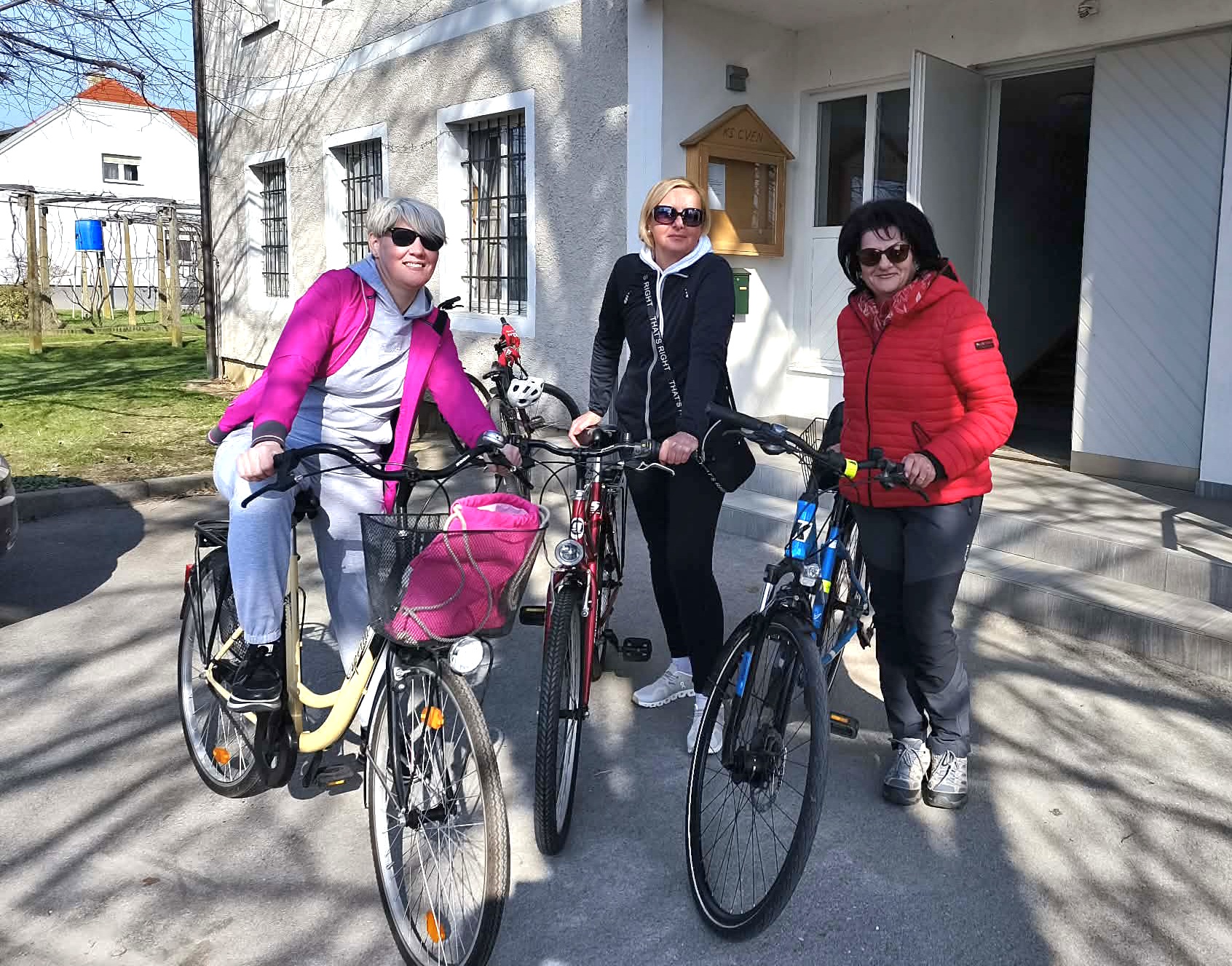 Tri udeleženke s kolesi pred Krajevno skupnostjo Cven